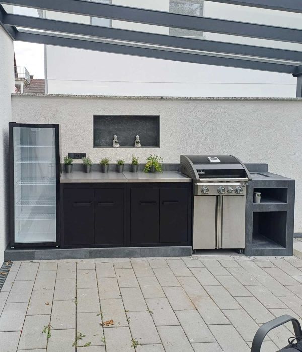 Überdachte Outdoorküche mit Grill, Spüle, dunklen Unterschränken und verputzter Rückwand