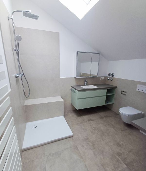 Badezimmer unter einer Dachschräge mit Dusche, grauen Bodenfliesen, grünem Waschtischunterschrank und wandhängender Toilette