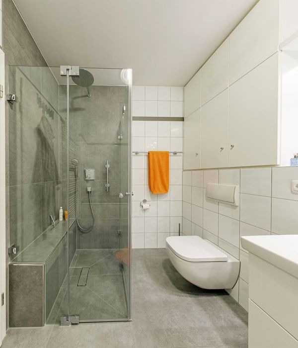 Helles Badezimmer mit bodengleicher Dusche, Glasabtrennung, grauen Bodenfliesen und wandhängender Toilette