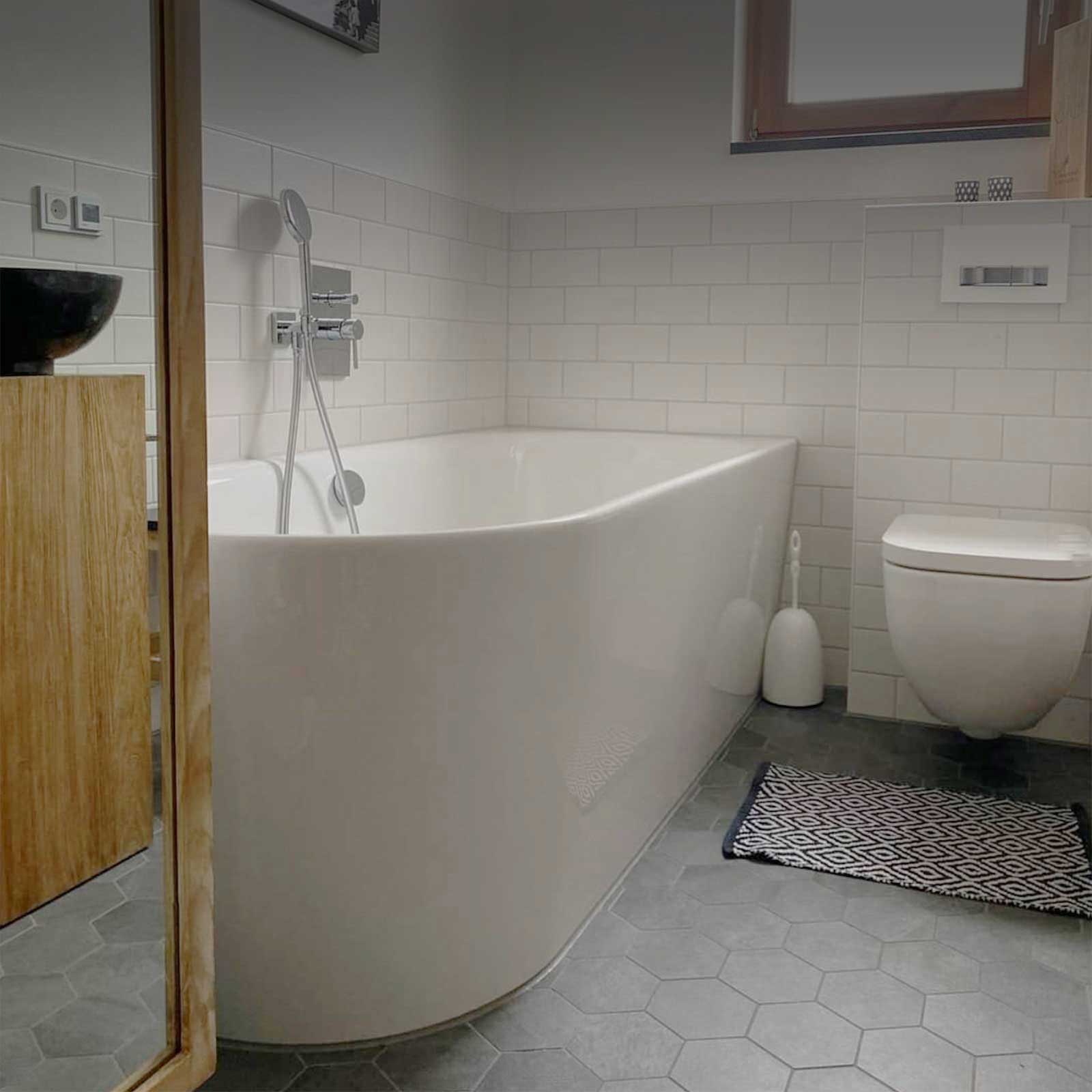Helles Badezimmer mit freistehender Badewanne, weißen Wandfliesen und grauen sechseckigen Bodenfliesen